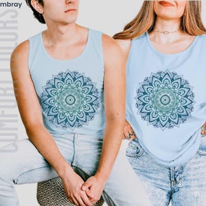 Man and woman in comfort colors 9360 chambray (light blue) tank top sleeveless tee with mandala graphic in blues and greens. Mandala contains hidden FDT, 8647, RESIST, and symbols of pro-choice.