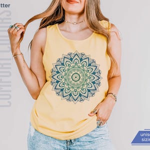 Woman in comfort colors 9360 butter yellow tank top sleeveless tee with mandala graphic in blues and greens. Mandala contains hidden FDT, 8647, RESIST, and symbols of pro-choice.