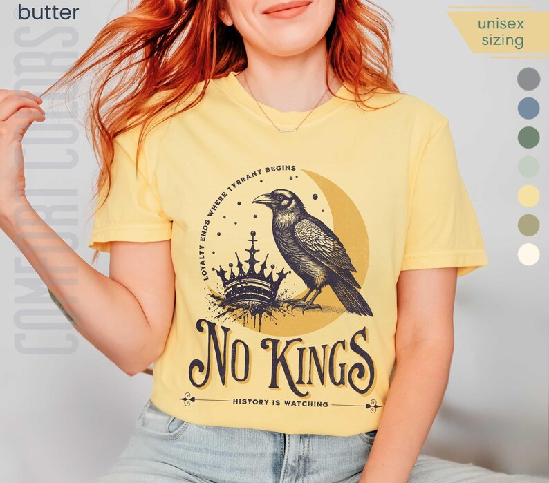 Woman wearing butter yellow Comfort Colors tees featuring a dark blue graphic of a raven, crown, and moon with No Kings – History is Watching design; Graphic is dark blue with goldenrod accents and crescent moon. unisex sizing displayed.