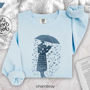 CHAMBRAY folded flat lay soft blue sweatshirt on white bedding with scrunchie and open novel, cozy reading day inspiration