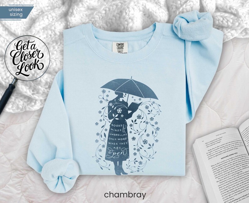 CHAMBRAY folded flat lay soft blue sweatshirt on white bedding with scrunchie and open novel, cozy reading day inspiration