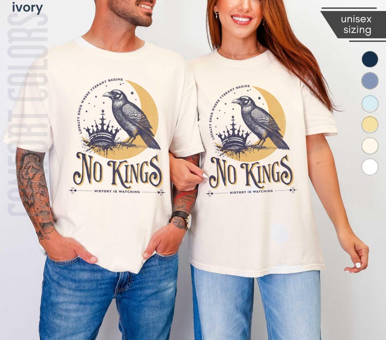 Man and woman wearing ivory Comfort Colors tees featuring a dark blue graphic of a raven, crown, and moon with No Kings – History is Watching design; Graphic is dark blue with goldenrod accents and crescent moon. unisex sizing displayed.