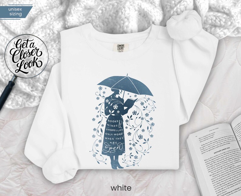 WHITE folded flat lay sweatshirt with literary umbrella design beside open book and cozy blanket, bookish home reading aesthetic