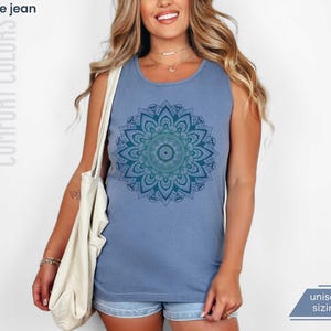 Woman in comfort colors 9360 blue jean (medium muted slate blue) tank top sleeveless tee with mandala graphic in blues and greens. Mandala contains hidden FDT, 8647, RESIST, and symbols of pro-choice.