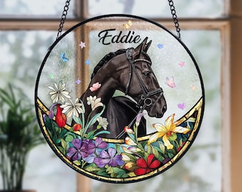Pode incluir: Decoração de janela redonda em vitral com um cavalo preto chamado "Eddie". O cavalo é cercado por flores coloridas, borboletas e estrelas. Uma corrente preta é anexada para pendurar.