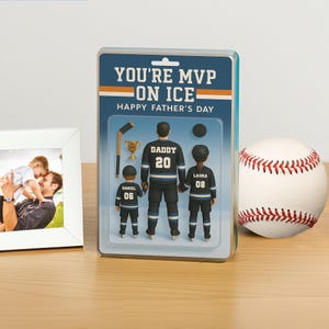 K&ouml;nnte beinhalten: Ein Geschenkset zum Vatertag mit einer Hockey-Figur mit dem Text "YOU'RE MVP ON ICE". Die Figur zeigt einen Vater und zwei Kinder in Hockey-Uniformen. Ein Baseball und ein gerahmtes Foto sind ebenfalls vorhanden.