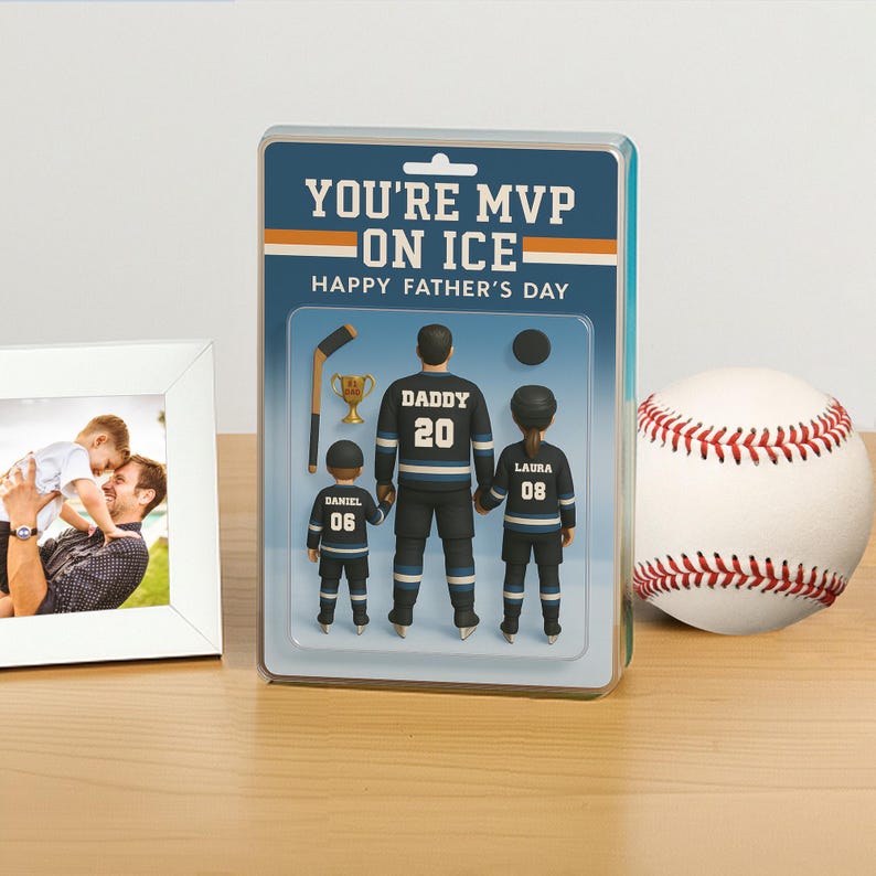 K&ouml;nnte beinhalten: Ein Geschenkset zum Vatertag mit einer Hockey-Figur mit dem Text "YOU'RE MVP ON ICE". Die Figur zeigt einen Vater und zwei Kinder in Hockey-Uniformen. Ein Baseball und ein gerahmtes Foto sind ebenfalls vorhanden.