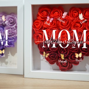 May include: A white frame with a heart-shaped arrangement of red roses. The word "MOM" is in the center of the roses, with the text "We love you" below it. There are names written around the roses, including "Jessica", "Karen", "Heidi", "Lisa", "Mariah", "Nicole", and "Erica".