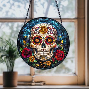 Puede incluir: Una ventana de vidrio coloreado que cuelga con un diseño de calavera de azúcar colorida. La calavera está rodeada de flores y hojas. El fondo es un mosaico azul.
