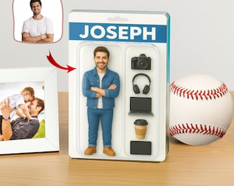 Puede incluir: Una figura de acción personalizada llamada JOSEPH, con una chaqueta vaquera y vaqueros, junto a una pelota de béisbol y una foto enmarcada. La figura incluye accesorios en miniatura: una cámara, auriculares, un portátil, una taza de café y una tableta. El embalaje tiene una pancarta azul con el nombre JOSEPH.