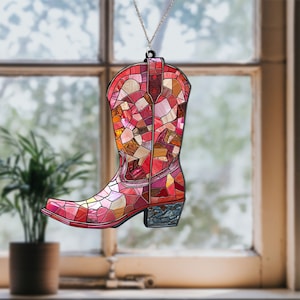 May include: A stained glass window hanging ornament shaped like a pink cowboy boot. The boot is decorated with a mosaic of pink, red, and orange glass pieces.