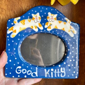 May include: Blue ceramic picture frame with white polka dots and the words "Good Kitty." The frame features two cartoon cats with orange and white markings. The frame has an oval opening for a photo.