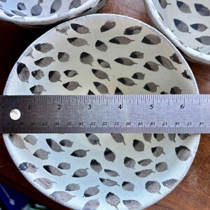 May include: A white ceramic bowl with a black leaf pattern. The bowl is 6 inches in diameter and is sitting on a wooden surface.
