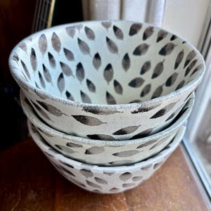 May include: Three white ceramic bowls with a black leaf pattern. The bowls are stacked on top of each other.
