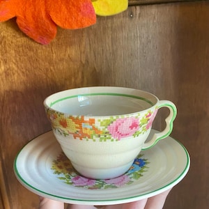 May include: A vintage teacup and saucer set with a floral pattern. The cup and saucer are white with a green trim and feature a colorful floral design.