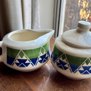 May include: A white ceramic creamer and sugar bowl set with a green, blue, and white geometric pattern.
