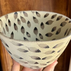 May include: A white ceramic bowl with a black and gray leaf pattern. The bowl is hand-painted and has a slightly textured surface.