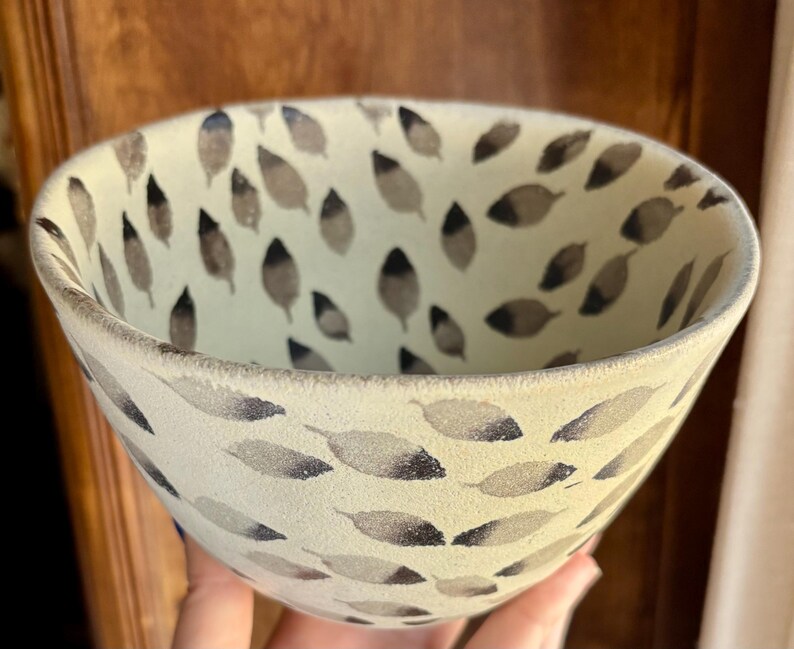 May include: A white ceramic bowl with a black and gray leaf pattern. The bowl is hand-painted and has a slightly textured surface.