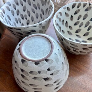 May include: Three white ceramic bowls with a black leaf pattern. The bowls are stacked on top of each other.