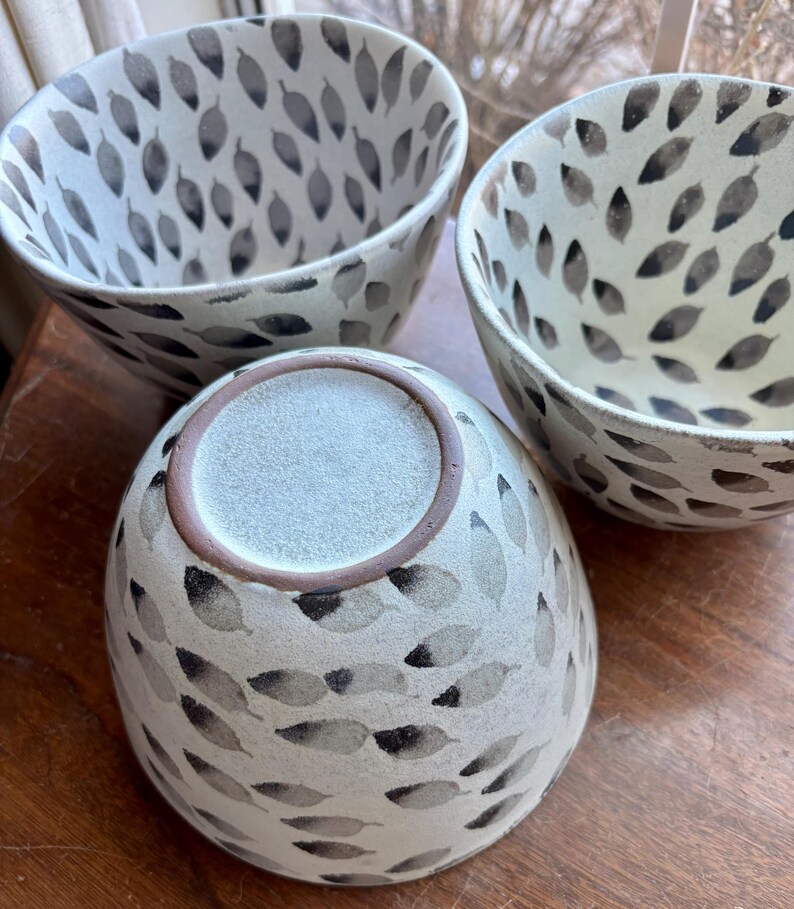 May include: Three white ceramic bowls with a black leaf pattern. The bowls are stacked on top of each other.