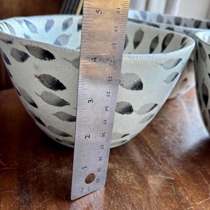 May include: A white ceramic bowl with a black and gray leaf pattern. The bowl is 4 inches in diameter.