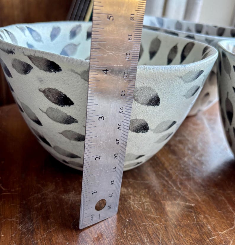 May include: A white ceramic bowl with a black and gray leaf pattern. The bowl is 4 inches in diameter.