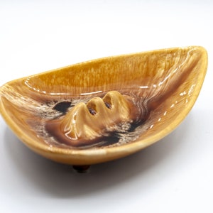 May include: A brown and white ceramic ashtray with a three-point design. The ashtray has a glossy finish and is shaped like a shallow bowl.