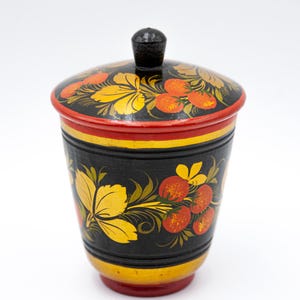 Peut inclure: Un récipient en bois noir avec un couvercle, peint avec des motifs floraux rouges, jaunes et verts. Le récipient est dans un style d'art populaire russe traditionnel.