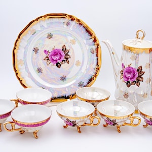Op de afbeelding: Een wit porseleinen theeservies met gouden rand en bloemmotieven. De set bevat een theepot, een serveerschaal en zes theekopjes met schoteltjes.