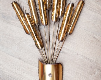 May include: A gold metal wall sculpture in the shape of a wheat stalk with multiple stalks and a curved base.