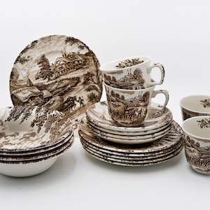 Può includere: Una collezione di stoviglie in ceramica marrone e bianca, tra cui piatti, ciotole, piattini e tazze da tè. I pezzi presentano un design paesaggistico dettagliato. Il set include un piatto da portata grande, diversi piatti piccoli e tazze e piattini.