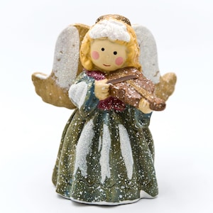 May include: A ceramic angel figurine with blonde hair, rosy cheeks, and a green dress playing a brown violin. The angel has gold wings dusted with glitter and wears a blue and red scarf. A festive holiday decoration.
