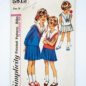 Könnte beinhalten: Simplicity Schnittmuster Nummer 5812, Größe 10, für ein Matrosenkleid mit Faltenrock. Das Schnittmuster zeigt drei Mädchen, die das Kleid in verschiedenen Farben tragen: blau, rot und weiß.