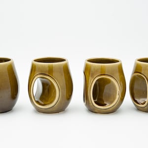 May include: Four olive green ceramic mugs with unique cut-out handles. The mugs are all the same size and shape, and they are arranged in a row on a white background.