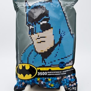 May include: Perler bead kit featuring a pixelated Batman design. The kit includes 3500 beads and a pattern. The packaging is a gray plastic bag with the Perler and DC Comics logos. The kit is 12+ and includes tweezers.