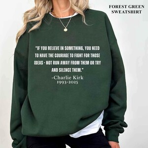 May include: Forest green sweatshirt with the quote "IF YOU BELIEVE IN SOMETHING, YOU NEED TO HAVE THE COURAGE TO FIGHT FOR THOSE IDEAS - NOT RUN AWAY FROM THEM OR TRY AND SILENCE THEM." by Charlie Kirk, 1993-2025. The text "FOREST GREEN SWEATSHIRT" is at the top.