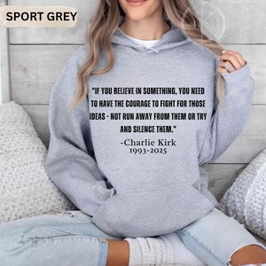 May include: Sport grey hoodie with the quote "IF YOU BELIEVE IN SOMETHING, YOU NEED TO HAVE THE COURAGE TO FIGHT FOR THOSE IDEAS - NOT RUN AWAY FROM THEM OR TRY AND SILENCE THEM." by Charlie Kirk, 1993-2025. The hoodie is a light grey color.