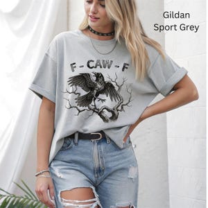 May include: A light gray t-shirt with a graphic of a raven perched on a tree branch, with the text "F-CAW-F" above the raven. The shirt is a Gildan Sport Grey.