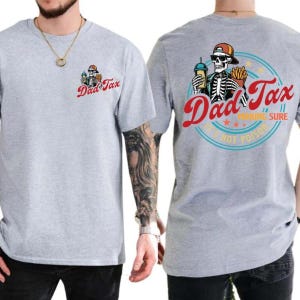 以下が含まれることがあります： 「Dad Tax」の文字と、前面と背面に骸骨のグラフィックがプリントされたライトグレーのTシャツ。背面のグラフィックは、飲み物とフライドポテトを持った骸骨で、「Making Sure It's Not Poison」の文字で囲まれています。