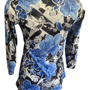 May include: A long-sleeved top featuring a collage of black and white images with large blue rose floral accents. The top has a scoop neck and is made of a lightweight, possibly sheer fabric. The design is repeated across the entire garment.