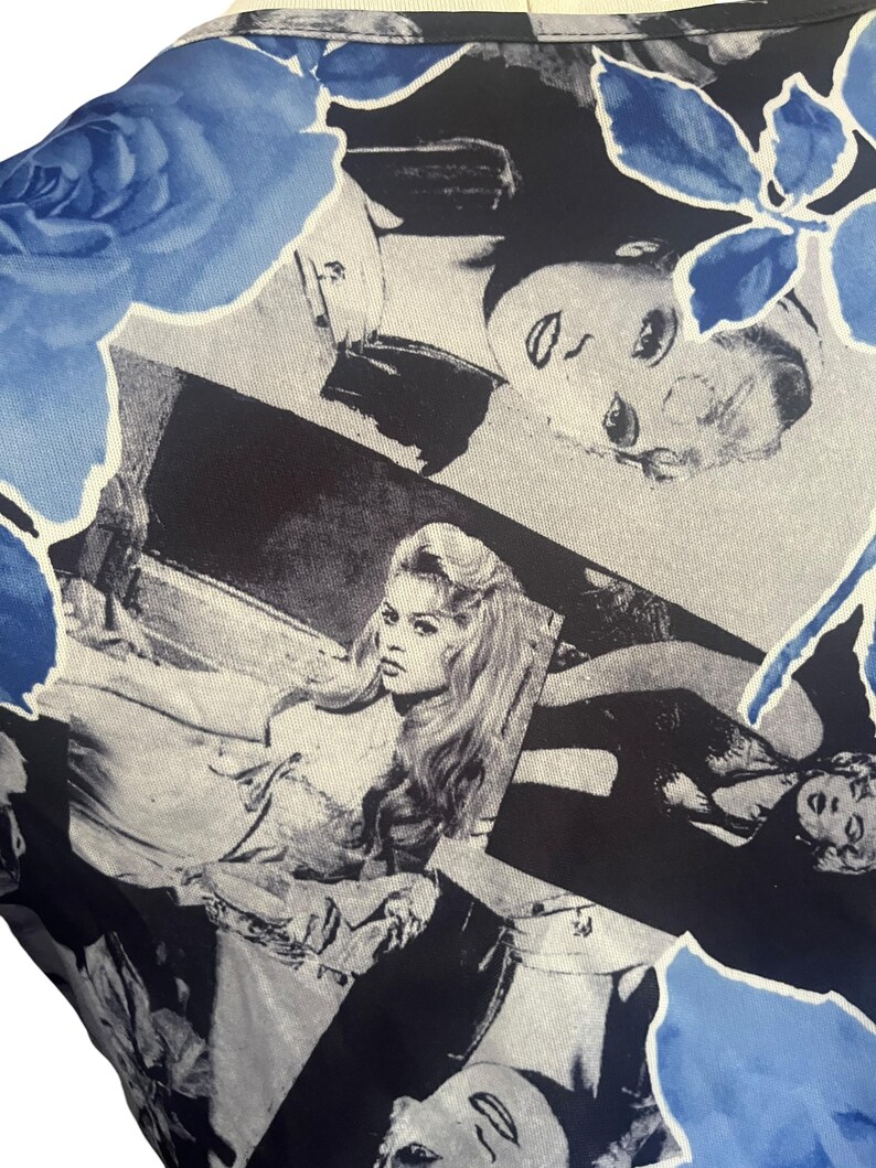May include: A close-up of a garment with a repeating pattern of black and white celebrity portraits and blue floral accents. The fabric has a silky sheen and a light cream-colored neckline.