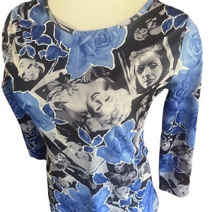 May include: A long-sleeved top featuring a collage of black and white vintage portraits and blue roses. The round-neck shirt has a fitted silhouette and is made of a soft, lightweight material. The floral and portrait design creates a unique and artistic look.