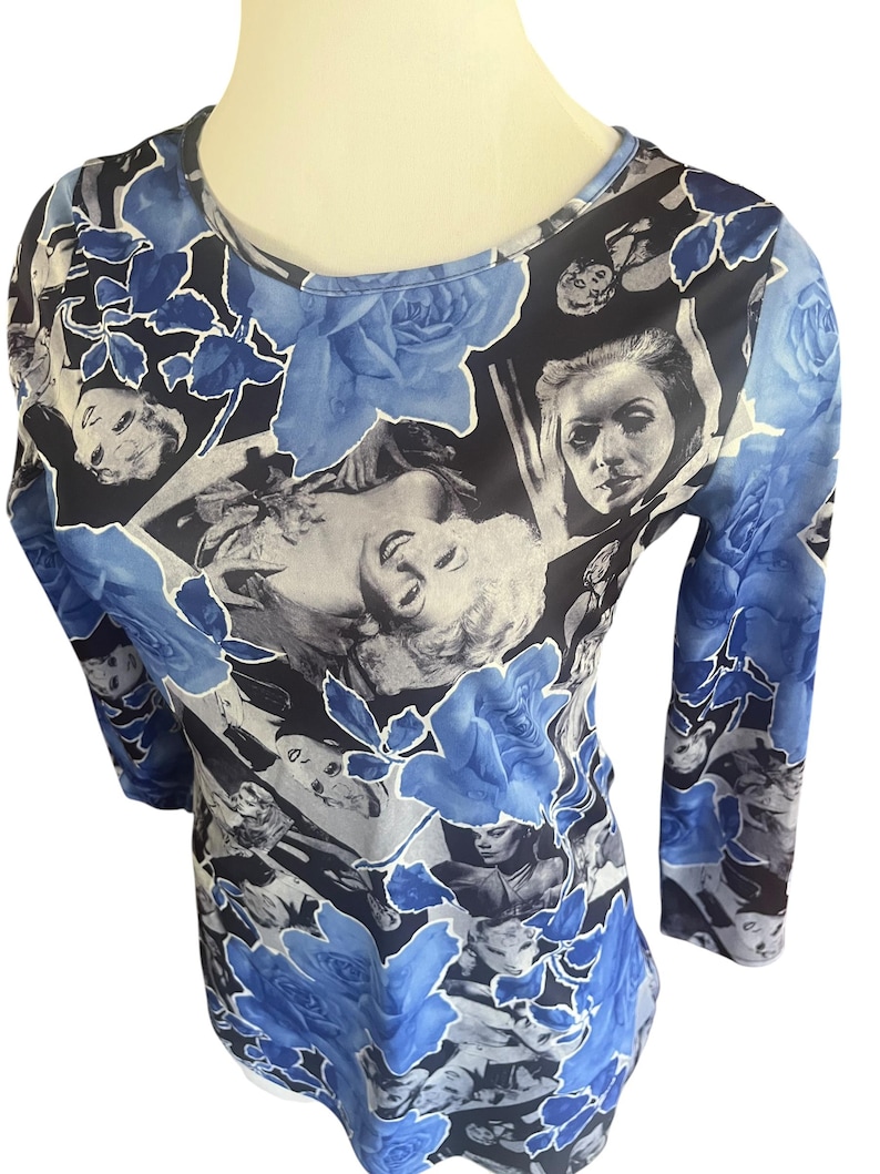May include: A long-sleeved top featuring a collage of black and white vintage portraits and blue roses. The round-neck shirt has a fitted silhouette and is made of a soft, lightweight material. The floral and portrait design creates a unique and artistic look.