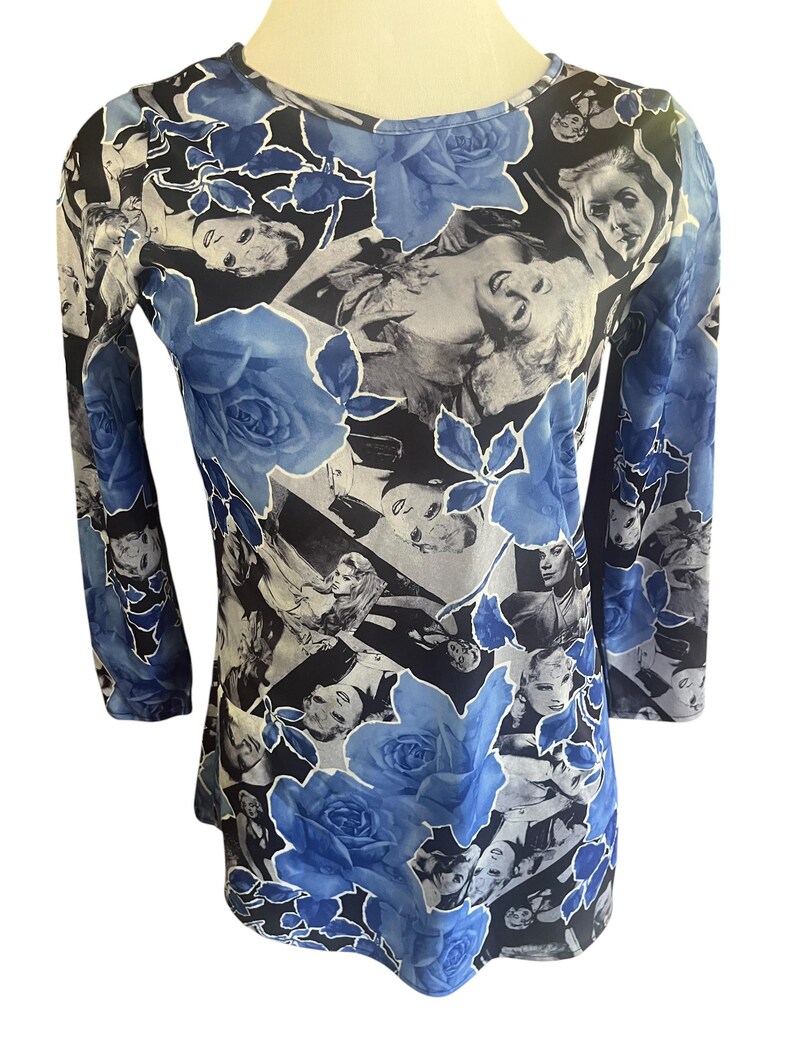 May include: Long-sleeved top with a unique design. The top features a pattern of black and white faces, blue roses, and a black background. The sleeves are three-quarter length, and the neckline is a scoop neck.