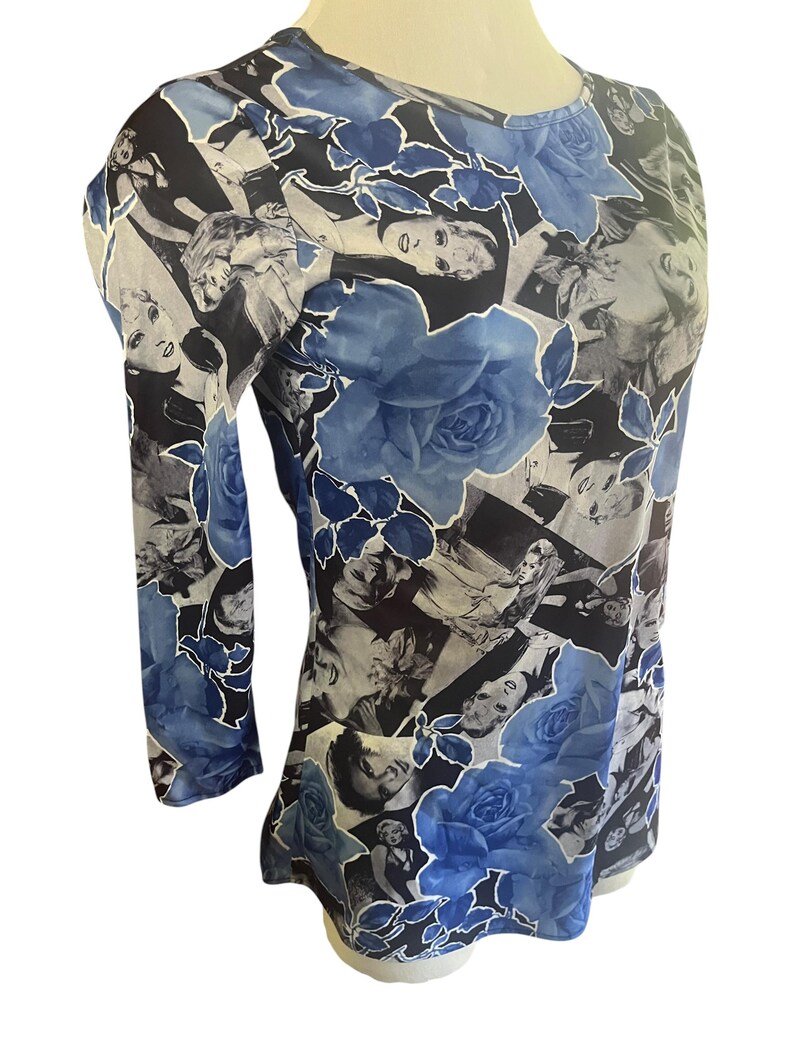 May include: A long-sleeved top featuring a collage of black and white images and large blue rose patterns. The top has a round neckline and a fitted silhouette, with the floral design adding a touch of elegance.