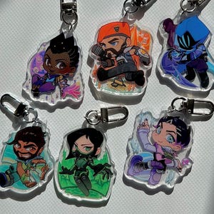 May include: A collection of six acrylic keychains featuring cartoon characters. Each keychain has a silver clasp and a unique character design with vibrant colors. The characters are set against a translucent, irregular background.