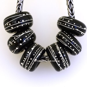 May include: Six black and white glass beads with a white paint splatter design. The beads are strung on a silver chain.