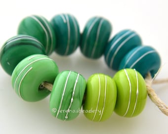 May include: A strand of green and blue glass beads with silver accents. The beads are strung on a natural twine cord.