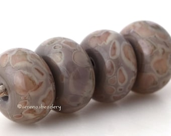 May include: Four round, patterned beads in shades of gray and brown are strung on a natural fiber cord. The beads have a speckled design, and the cord is a light tan color. The beads are smooth and have a glossy finish.