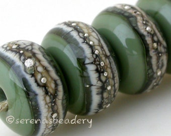 May include: A string of green glass beads with a speckled, patterned design in white and black. The beads are round with a hole through the centre, strung on a natural fibre cord. The beads have a glossy finish.